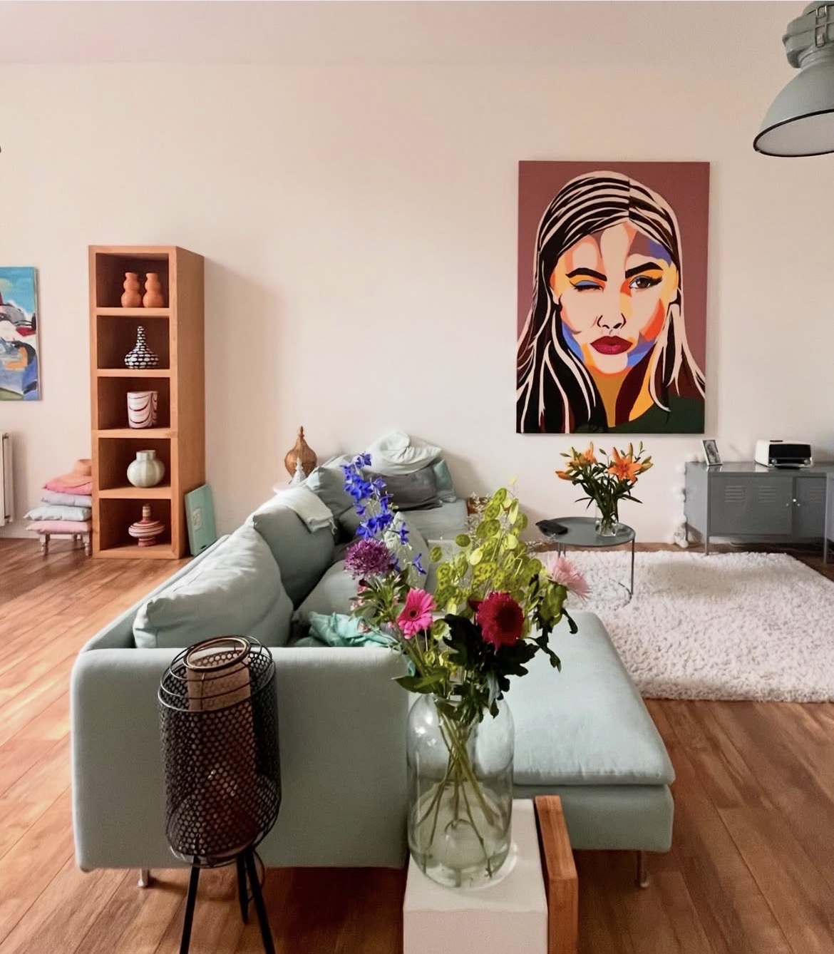 Commissioned portrait of a winking woman on a warm rose background, hanging above a sideboard in a living room