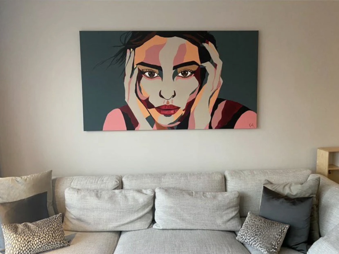 A finished colourful portrait painting hanging in a bright loft interior