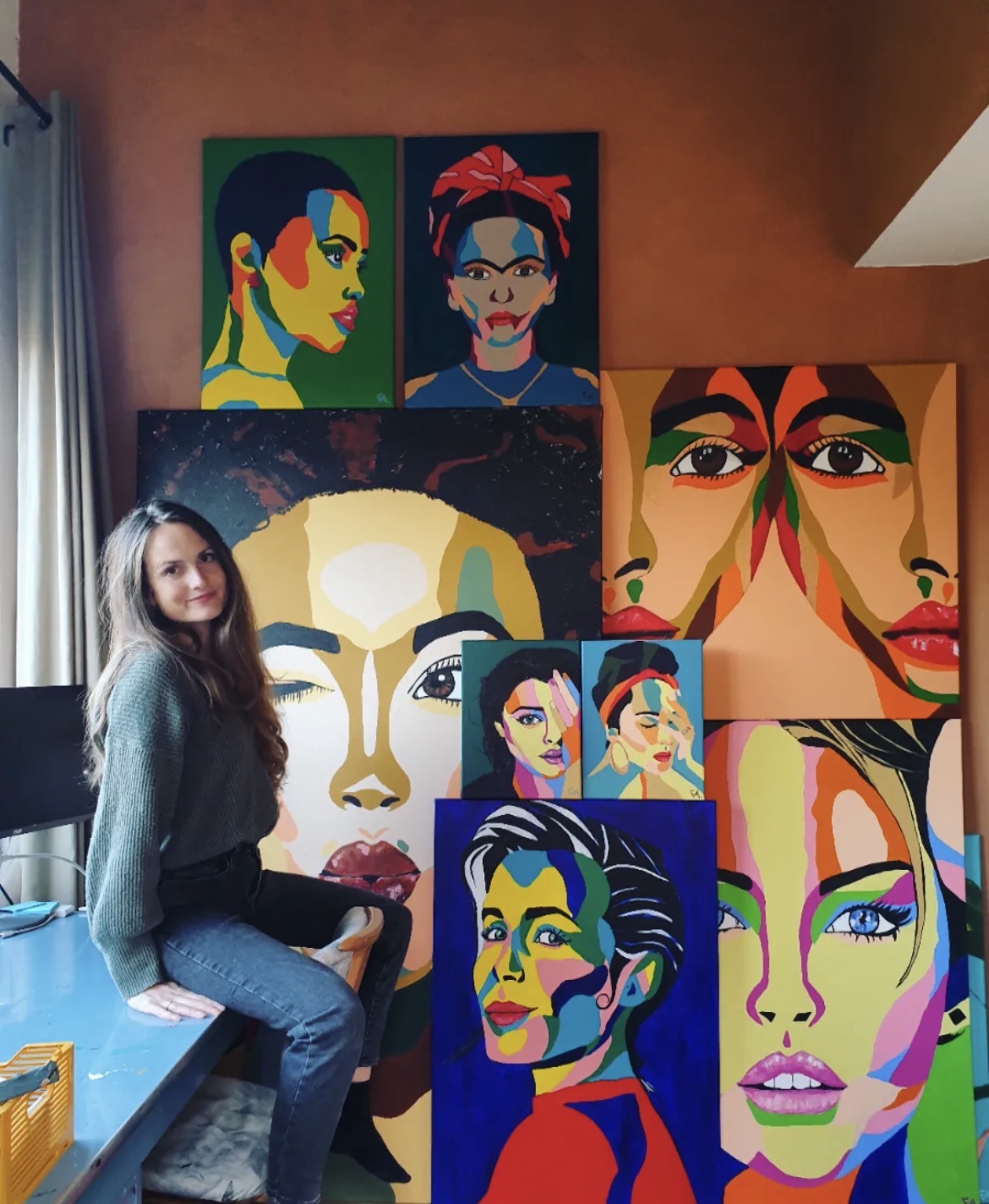 Fabienne in her studio surrounded by a wall of colourful portrait paintings